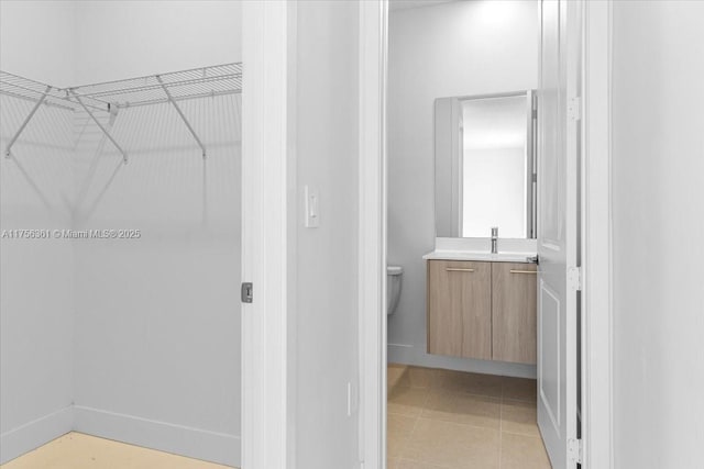 bathroom featuring a walk in closet, toilet, tile patterned flooring, baseboards, and vanity