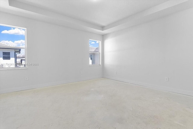 unfurnished room featuring a tray ceiling, baseboards, and concrete flooring