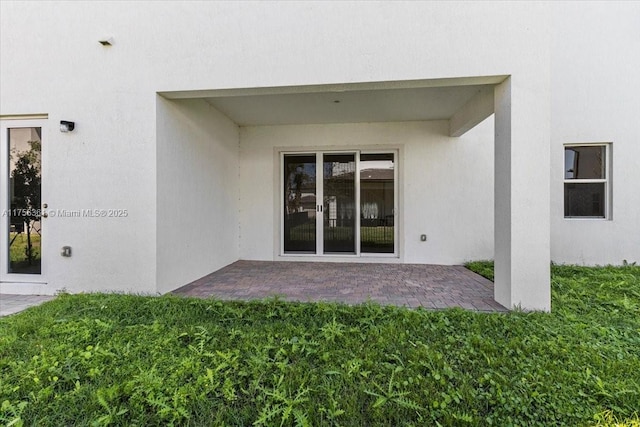 doorway to property featuring a patio, a yard, and stucco siding