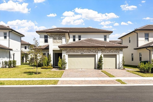 prairie-style house featuring decorative driveway, a front yard, an attached garage, and a tile roof