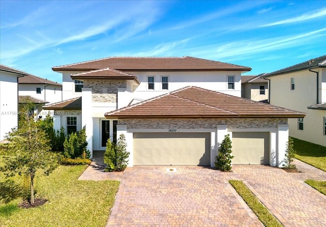 view of front facade featuring decorative driveway, a tile roof, an attached garage, and a front yard