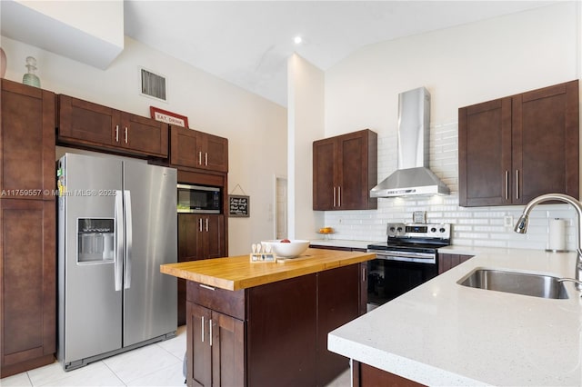 kitchen featuring a sink, wood counters, a kitchen island, appliances with stainless steel finishes, and wall chimney range hood