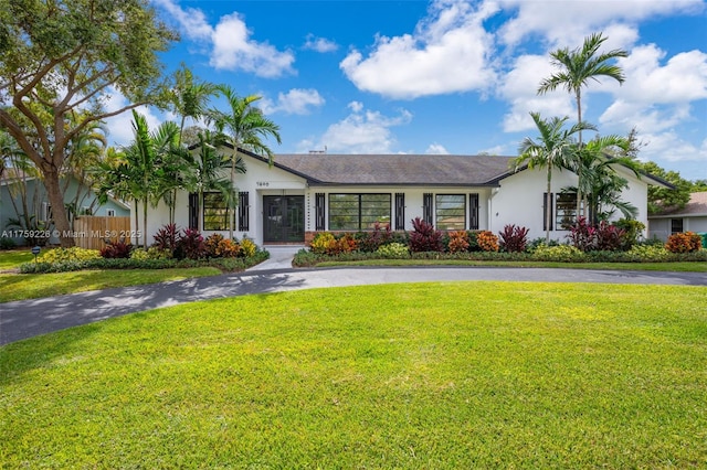 ranch-style home featuring driveway, a front yard, fence, and stucco siding