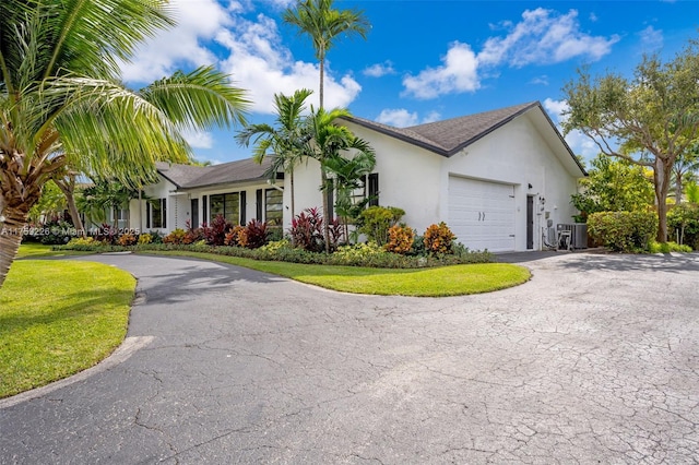 view of front of property featuring aphalt driveway, cooling unit, a garage, stucco siding, and a front lawn