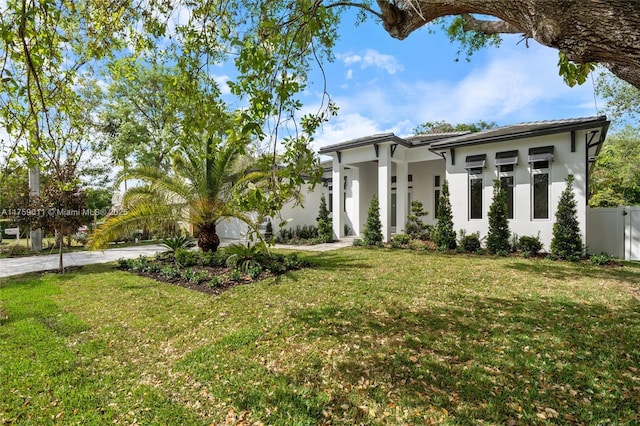 view of front of house with stucco siding, driveway, a front lawn, and fence