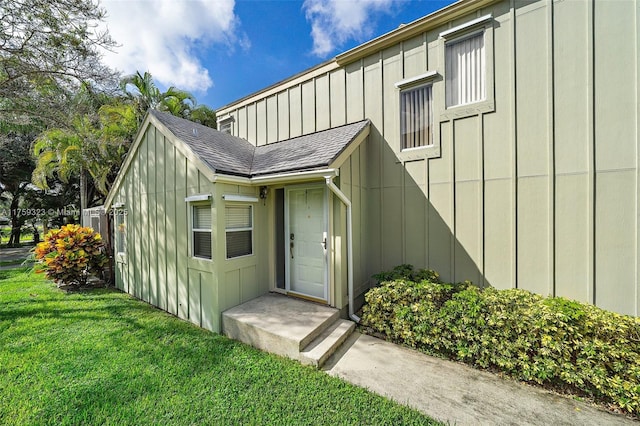 property entrance featuring a lawn, board and batten siding, and roof with shingles