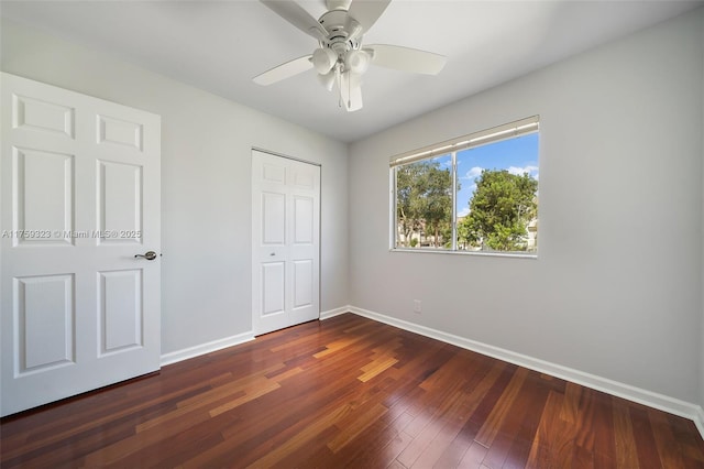 unfurnished bedroom with a closet, baseboards, dark wood-style floors, and a ceiling fan