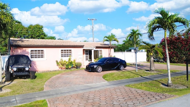 single story home with stucco siding, a tiled roof, a front yard, and fence