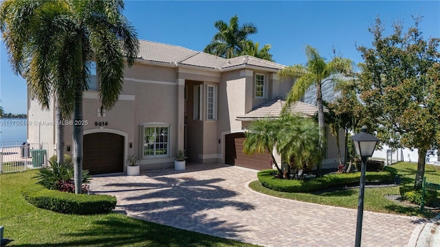 mediterranean / spanish-style house with stucco siding, a tile roof, decorative driveway, fence, and a garage