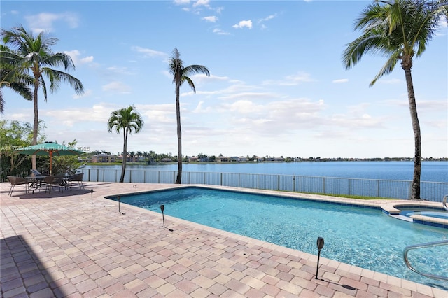 view of pool with a patio area, fence, a water view, and a pool with connected hot tub