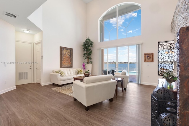 living area with visible vents, a water view, a high ceiling, and dark wood-style floors