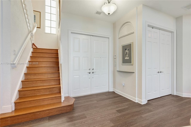 entryway with visible vents, stairway, dark wood-type flooring, and baseboards