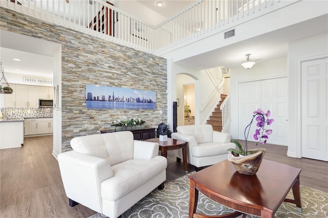 living room featuring stairway, wood finished floors, visible vents, arched walkways, and a towering ceiling