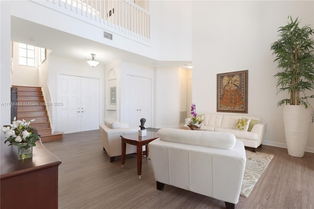 living room with stairway, a high ceiling, visible vents, and wood finished floors