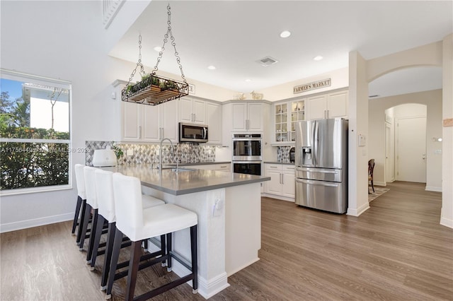 kitchen featuring visible vents, a peninsula, arched walkways, a sink, and stainless steel appliances