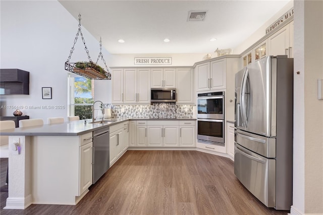 kitchen featuring visible vents, light wood-style flooring, a peninsula, stainless steel appliances, and a sink