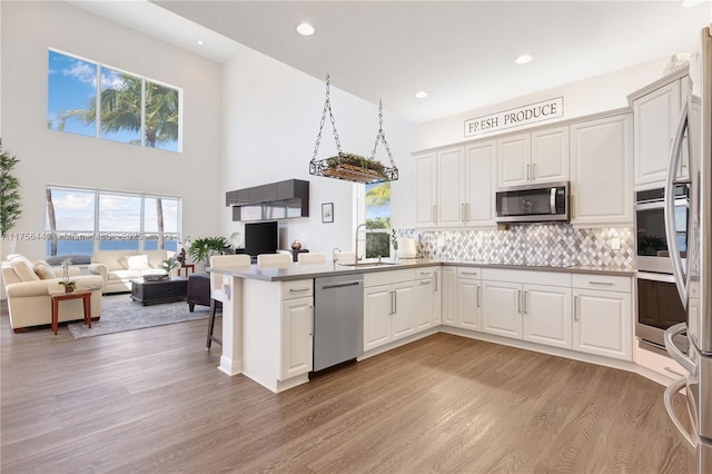 kitchen featuring a sink, open floor plan, a peninsula, appliances with stainless steel finishes, and light wood finished floors