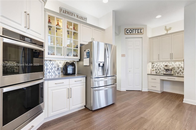 kitchen featuring white cabinetry, glass insert cabinets, light wood-style flooring, stainless steel appliances, and built in study area