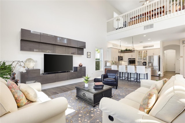 living room with visible vents, wood finished floors, recessed lighting, arched walkways, and a high ceiling