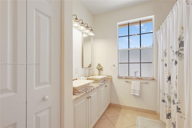 full bath featuring tile patterned flooring, double vanity, baseboards, and a sink