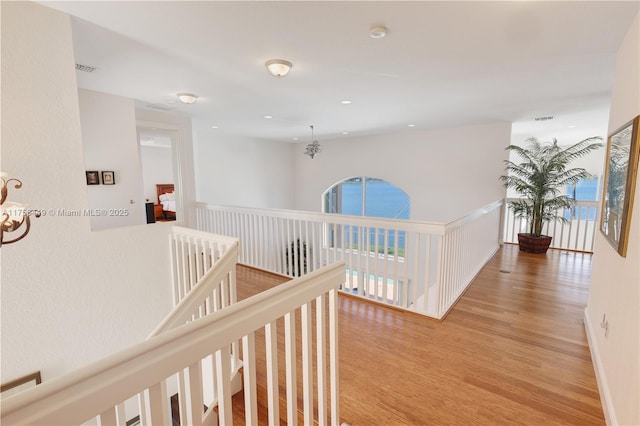 corridor featuring wood finished floors, visible vents, baseboards, recessed lighting, and an upstairs landing