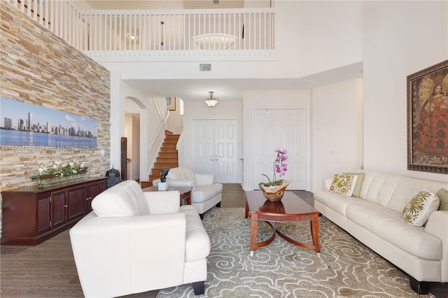 living area with visible vents, stairway, a towering ceiling, wood finished floors, and arched walkways