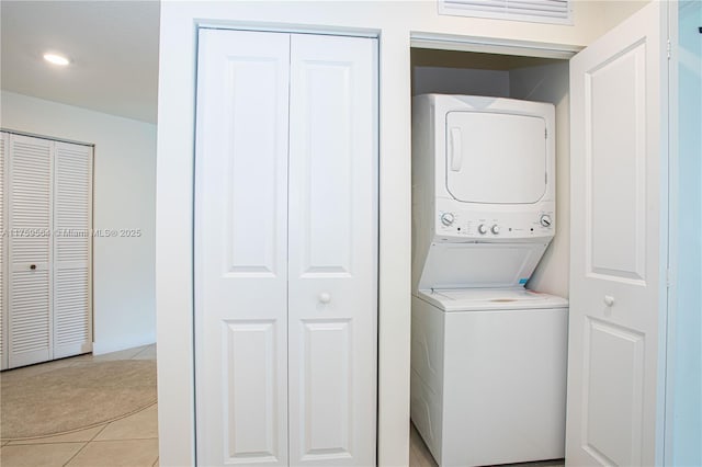 washroom featuring stacked washer / drying machine, visible vents, light tile patterned flooring, laundry area, and baseboards