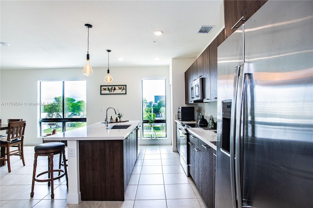 kitchen with stainless steel appliances, light countertops, light tile patterned flooring, a sink, and dark brown cabinetry