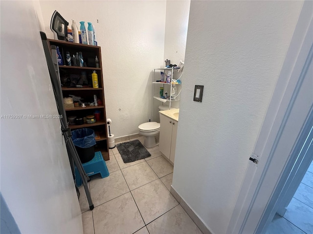 bathroom with a textured wall, toilet, vanity, baseboards, and tile patterned floors