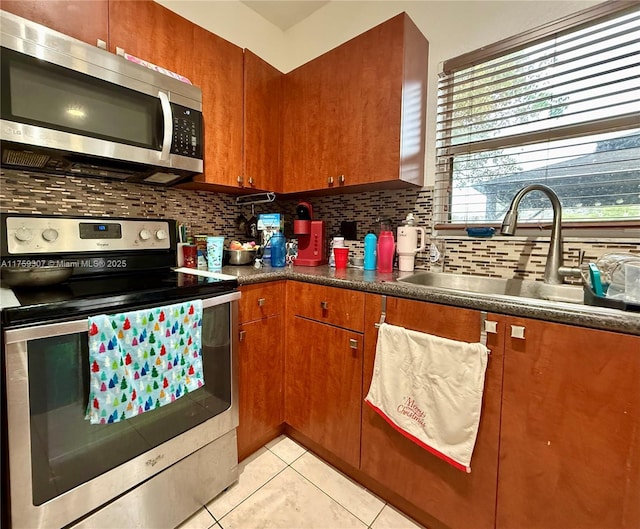 kitchen featuring brown cabinets, stainless steel appliances, tasteful backsplash, light tile patterned flooring, and a sink