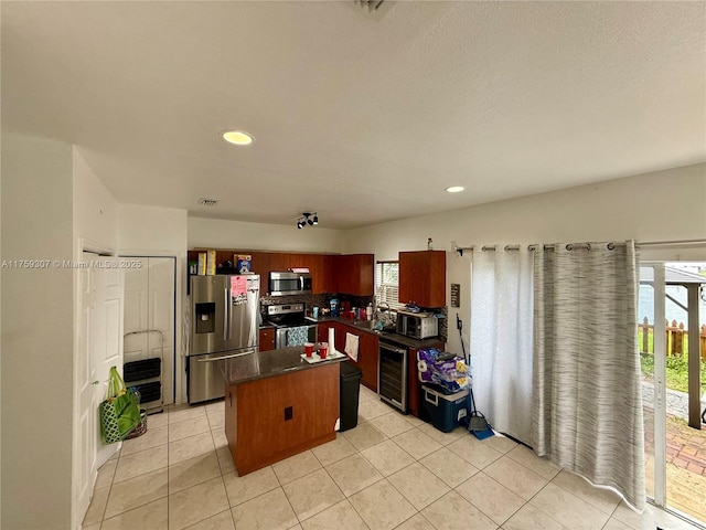 kitchen with light tile patterned floors, stainless steel appliances, dark countertops, a kitchen island, and beverage cooler