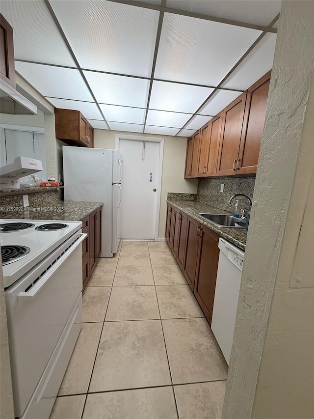 kitchen featuring light tile patterned floors, dark countertops, decorative backsplash, a sink, and white appliances