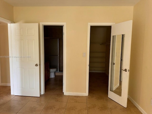 unfurnished bedroom featuring light tile patterned floors, a spacious closet, baseboards, and a closet