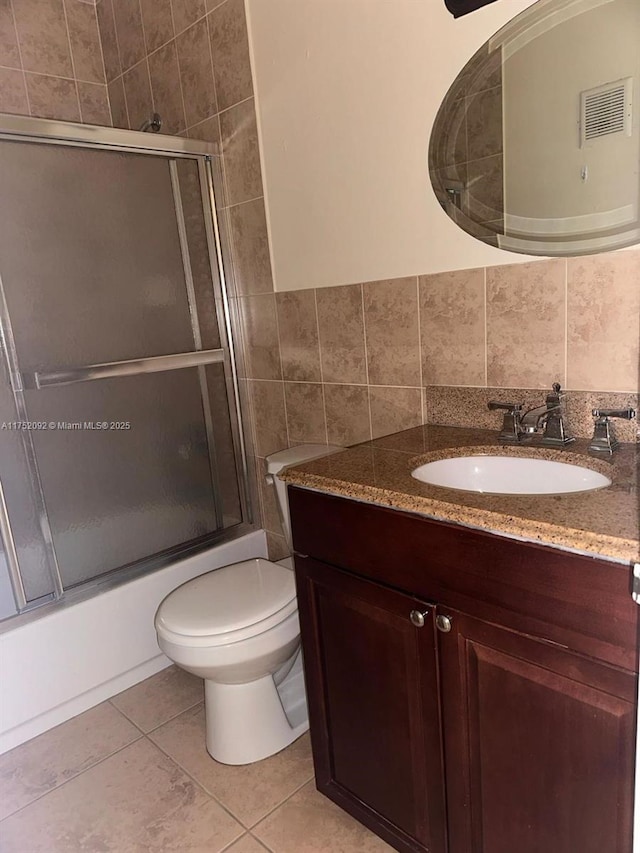 full bath featuring shower / bath combination with glass door, tile walls, toilet, vanity, and tile patterned flooring