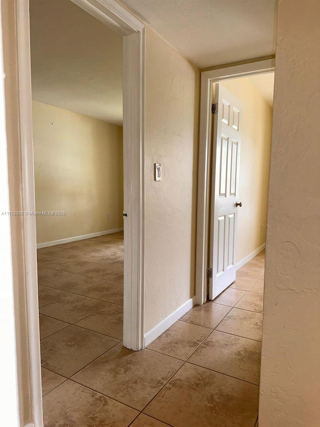 hallway featuring tile patterned floors, baseboards, and a textured wall