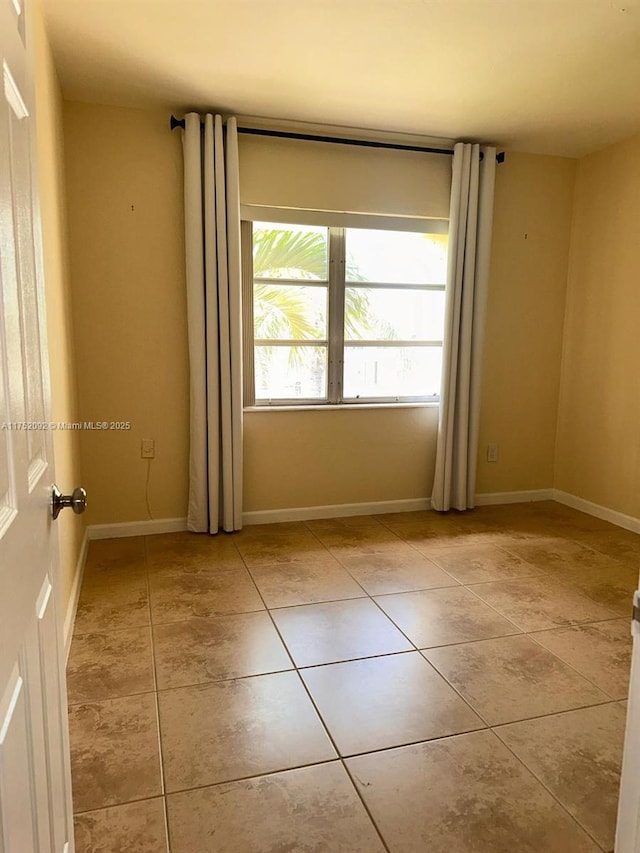 empty room featuring baseboards and light tile patterned floors