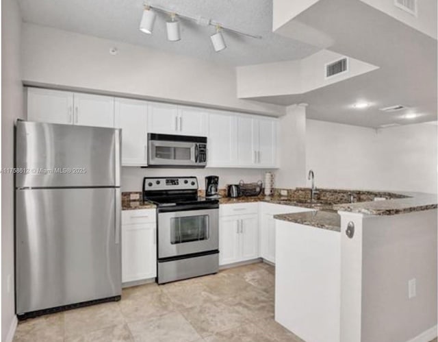 kitchen featuring dark stone counters, stainless steel appliances, a sink, and white cabinets