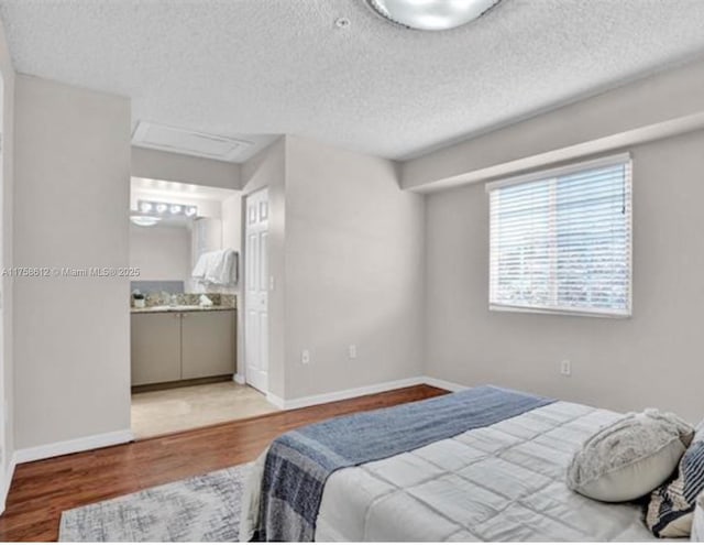 bedroom featuring ensuite bath, a textured ceiling, baseboards, and wood finished floors