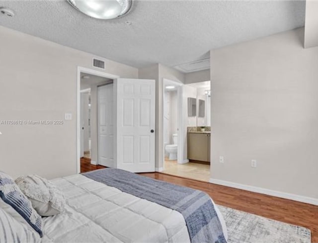 bedroom with baseboards, visible vents, connected bathroom, wood finished floors, and a textured ceiling