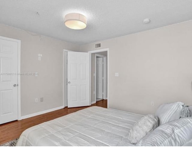 bedroom with a textured ceiling, wood finished floors, visible vents, and baseboards