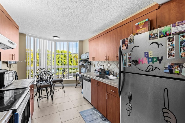 kitchen featuring tile countertops, light tile patterned floors, a sink, appliances with stainless steel finishes, and backsplash