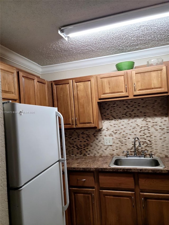 kitchen featuring ornamental molding, a sink, dark countertops, freestanding refrigerator, and decorative backsplash