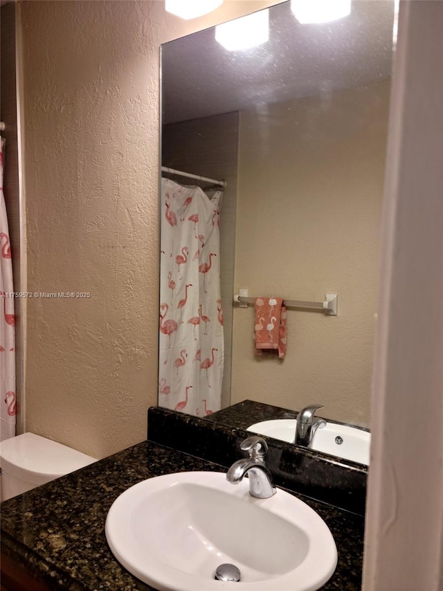 full bathroom featuring vanity, curtained shower, toilet, and a textured wall