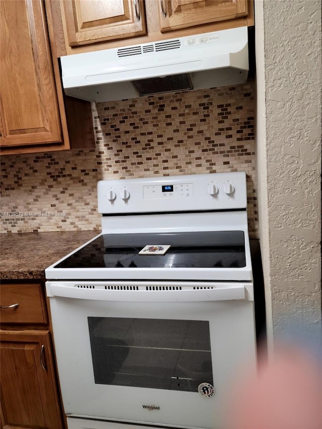 details featuring dark countertops, white electric range, tasteful backsplash, and under cabinet range hood