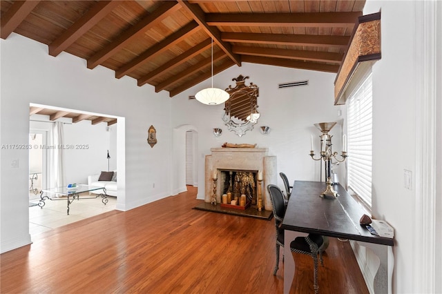 living room with visible vents, arched walkways, a fireplace with raised hearth, wooden ceiling, and wood finished floors