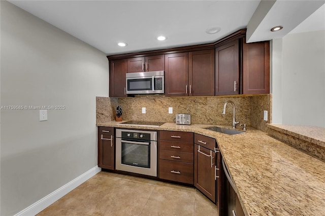 kitchen featuring decorative backsplash, appliances with stainless steel finishes, a sink, light stone countertops, and baseboards