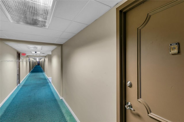 corridor featuring a paneled ceiling, baseboards, visible vents, and carpet flooring