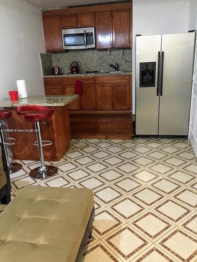 kitchen with appliances with stainless steel finishes, brown cabinetry, decorative backsplash, and light floors