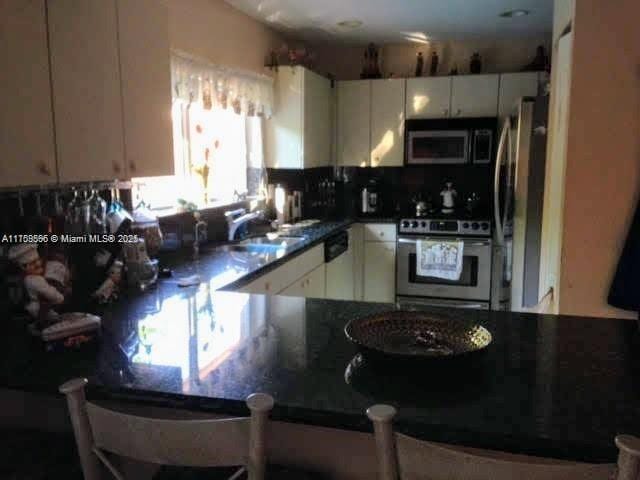 kitchen with a peninsula, a sink, white cabinetry, appliances with stainless steel finishes, and dark countertops