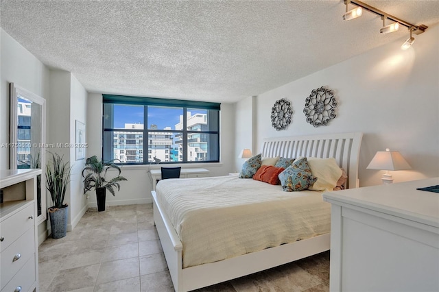 bedroom with a textured ceiling, light tile patterned floors, rail lighting, and baseboards